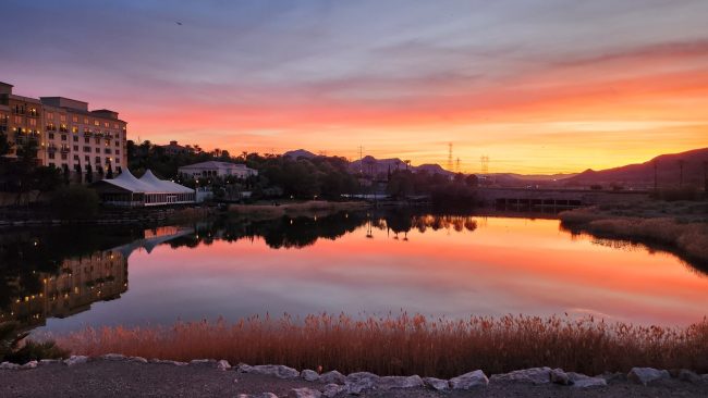 Sunset over Lake Las Vegas with homes and hotels in the background beneath a colorful evening sky.