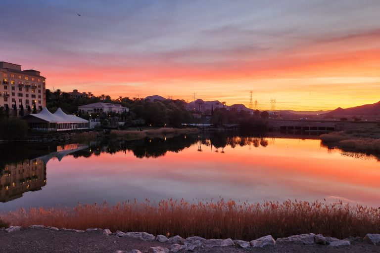 Sunset over Lake Las Vegas with homes and hotels in the background beneath a colorful evening sky.